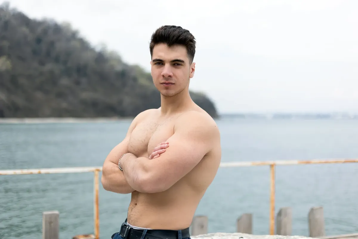 Young muscular man with crossed arms posing confidently on a shore.