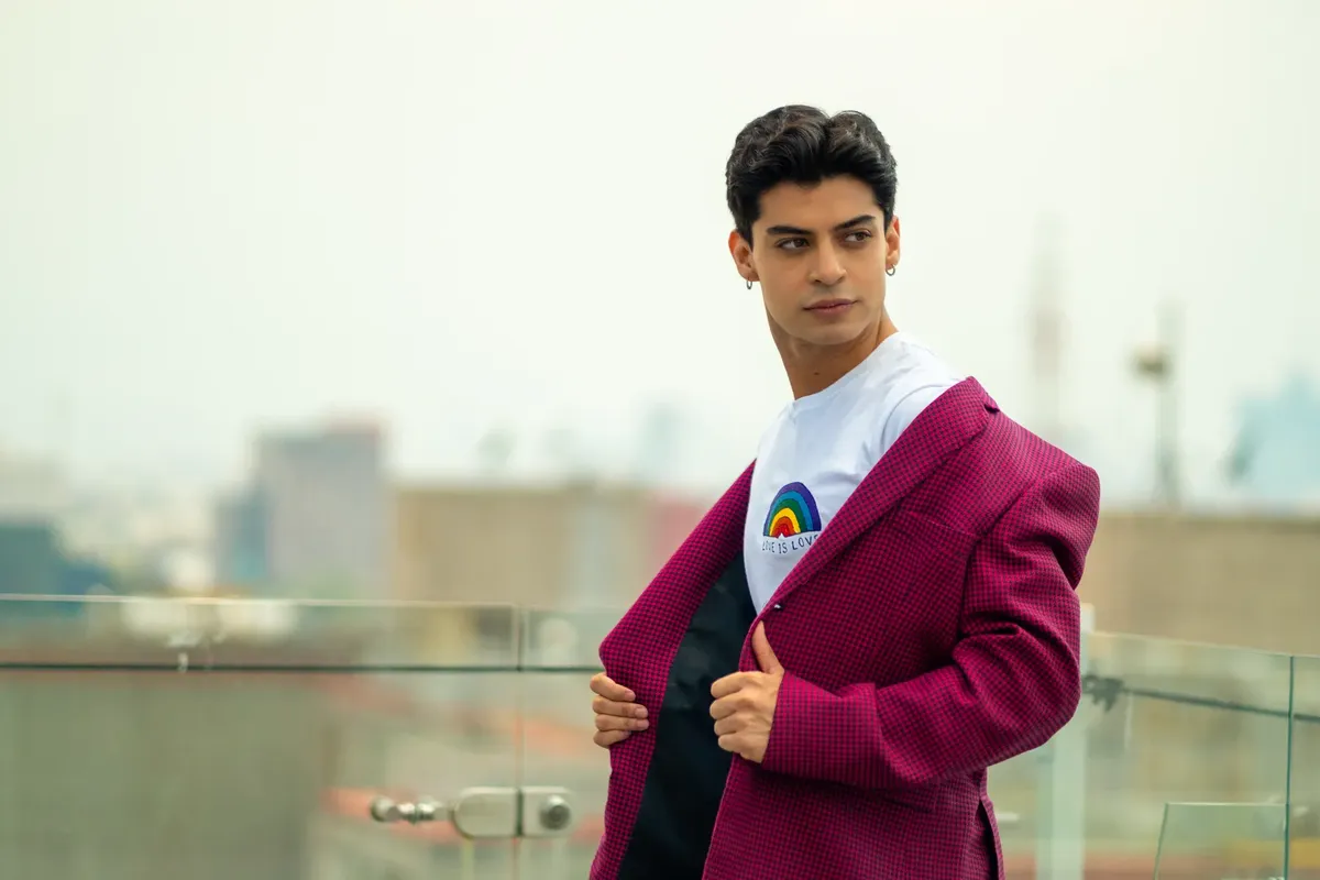 Confident man in vibrant outfit with rainbow emblem stands in Mexico City. Elegant and modern.