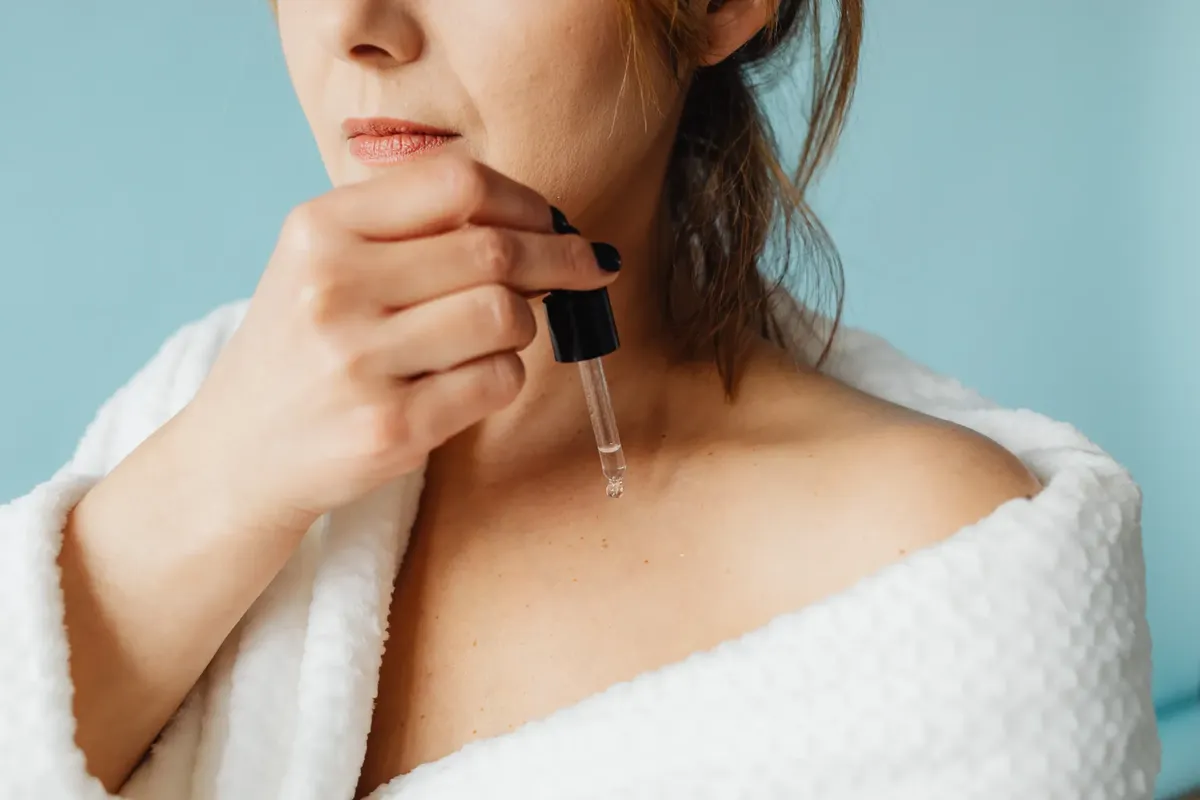 Close-up of a woman in a bathrobe applying serum for skincare routine.