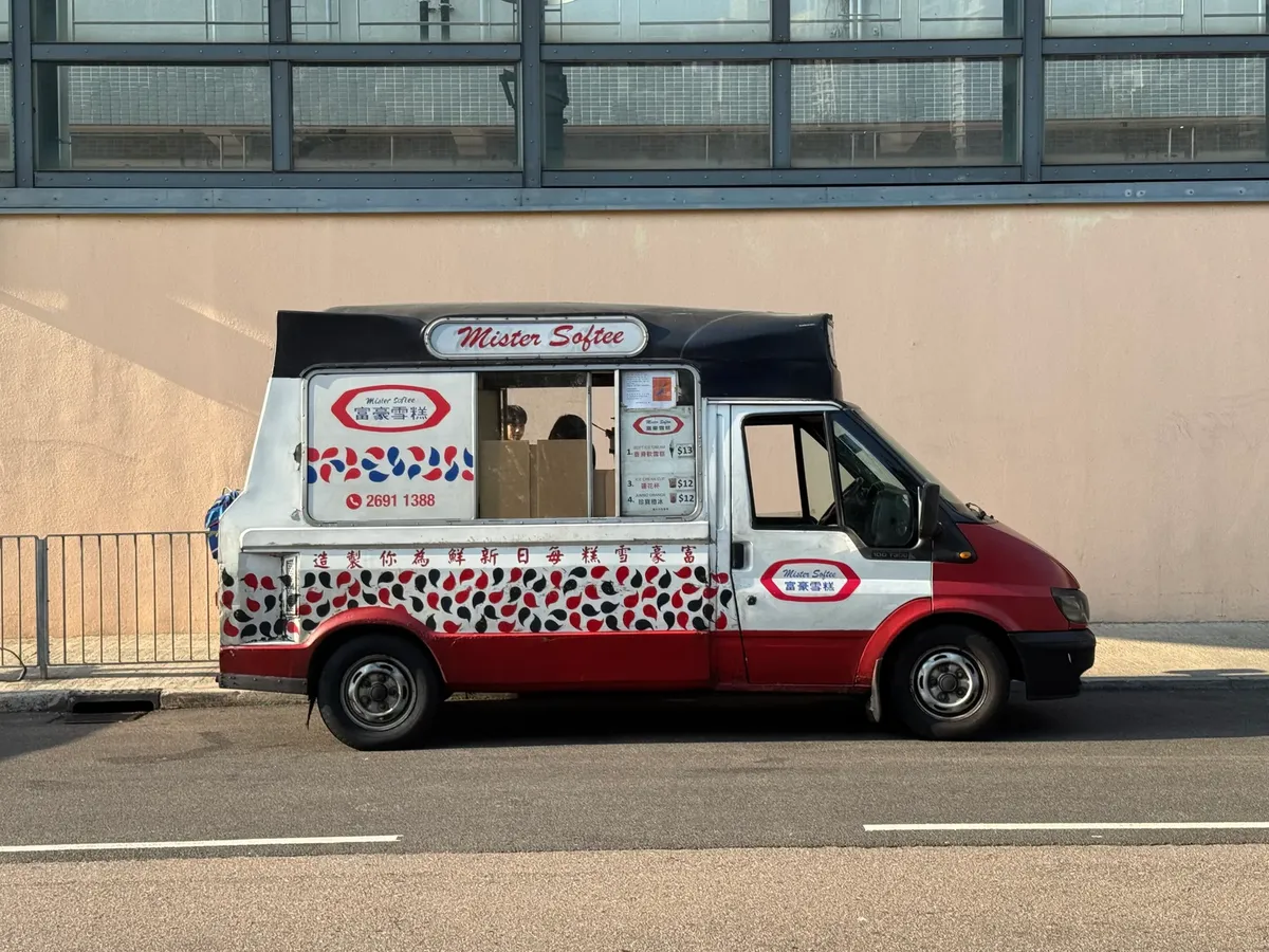 一輛懷舊的Mister Softee冰淇淋車停在都市街道旁，準備在陽光明媚的天氣下提供冷飲。